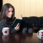 woman sitting at a table reading interesting book